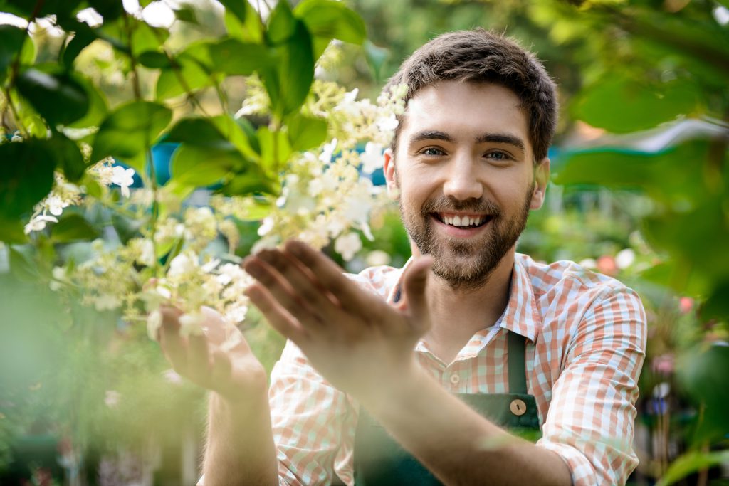 Young handsome cheerful gardener smiling, taking care of flowers.